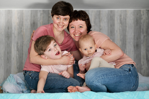 A young homosexual lesbian couple with two children at home, on the bed. They hug and play.