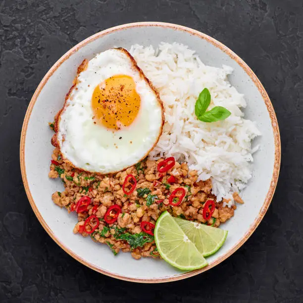 Photo of Pad Krapow Gai - Thai Basil Chicken with Rice and fried Egg black slate background. Pad Krapow is Thai cuisine dish with minced chicken or pork meat, basil, soy and oyster sauces. Thai Food.
