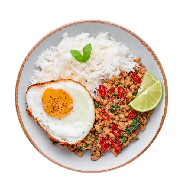Photo of Pad Krapow Gai - Thai Basil Chicken with Rice and fried Egg isolated on white background. Pad Krapow is Thai cuisine dish with minced chicken or pork meat, basil, soy and oyster sauces. Thai Food.