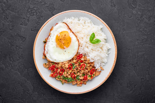 istock Pad Krapow Gai - Thai Basil Chicken with Rice and fried Egg black slate background. Pad Krapow is Thai cuisine dish with minced chicken or pork meat, basil, soy and oyster sauces. Thai Food Copy space 1216943106