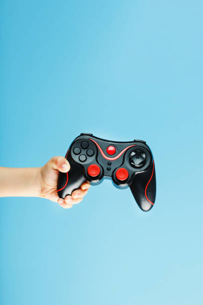 istock A gamepad on a blue background holds a child's hand as a weapon. Minimalistic creative concept of the younger generation of gamers. 1216943118