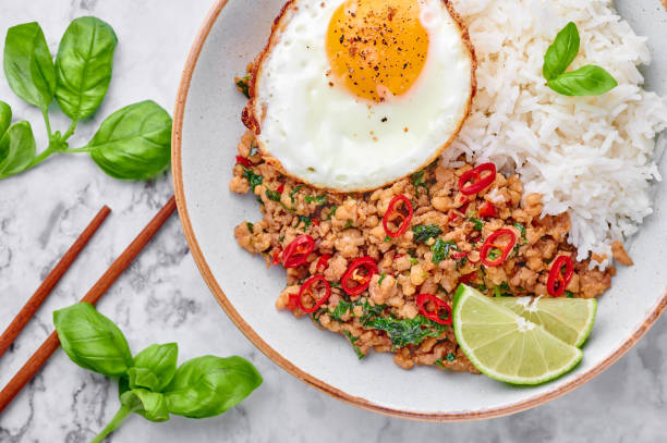 istock Pad Krapow Gai - Thai Basil Chicken with Rice and fried Egg on white marble background. Pad Krapow is Thai cuisine dish with minced chicken or pork meat, basil, soy and oyster sauces. Thai Food. 1216943199