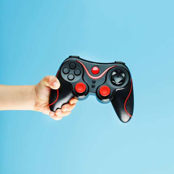 istock A gamepad on a blue background holds a child's hand as a weapon. Minimalistic creative concept of the younger generation of gamers. 1216945130
