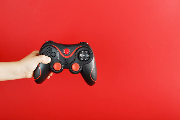 istock A child's hand holds a gamepad on a red background. Free space, minimalistic creative concept of the Younger generation of gamers. 1216945172