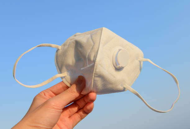 istock Hand holding surgical N95 mask with blue sky background 1216946513