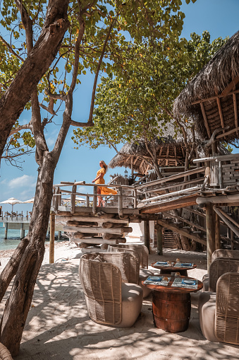 Woman standing in rustic driftwood Treehouse designed in Balinese outdoor living Architecture on tropical Maldives Island.