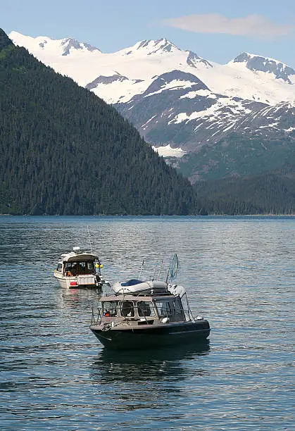Two fishing boats in a bay surrounded by snow-capped mountains.