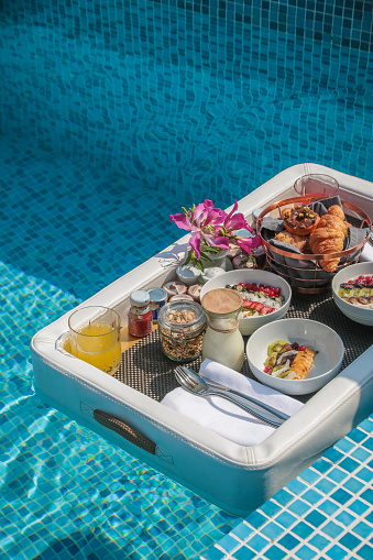 Luxurious Floating Breakfast served on floating leather tray in Swimming Pool, offering a variety of breakfast items such a s bowls, pastries and juices