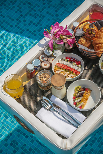 Luxurious Floating Breakfast served on floating leather tray in Swimming Pool, offering a variety of breakfast items such a s bowls, pastries and juices