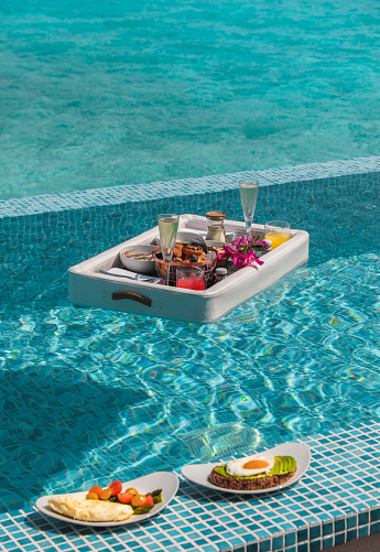 Luxurious Floating Breakfast served on floating leather tray in Swimming Pool by the sea, offering a variety of breakfast items such a s bowls, pastries and juices