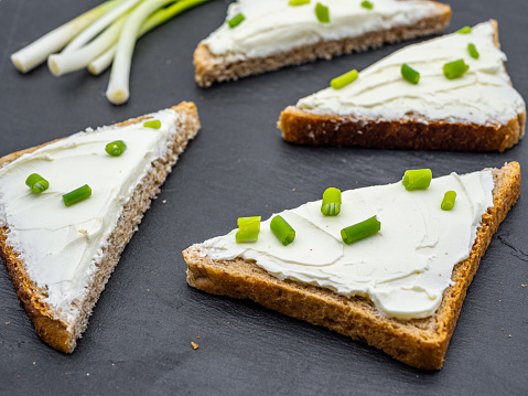 slices of bread with cream cheese spread and fresh 
green onion on black slate breakfast shack concept