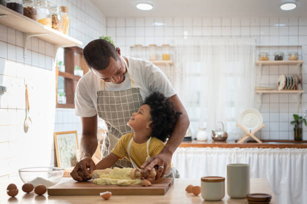 famille africaine heureuse de sourire dans la cuisson de tabliers et la pâte de pétrissage sur la table en bois. - two parent family indoors home interior domestic kitchen photos et images de collection