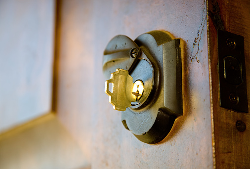 A golden hued key in a lock on a hardwood door.  Narrow depth of field with focus on the key.