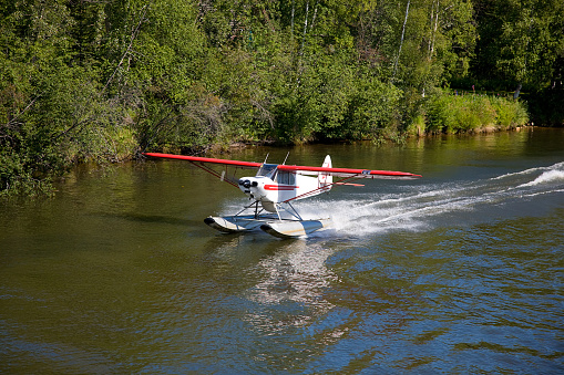 A small red and white float plane taking off of water in a wilderness setting.