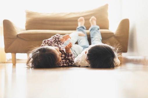 Asian older brother and younger sister lying down on floor in the living room.