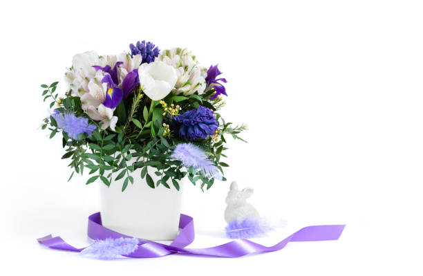 Easter composition. Spring flowers with feathers, purple ribbon and Easter Bunny on a white background. Copy space. Side view.