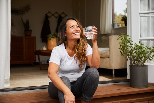 Mature woman laughing while sitting alone on her patio steps outside drinking a glass of water