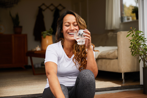 Mature woman laughing with her eyes closed while sitting on her patio steps drinking a glass of water