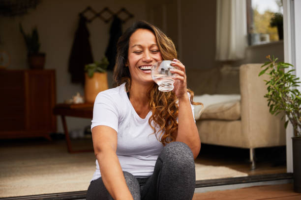 Laughing mature woman drinking water on her patio Mature woman laughing with her eyes closed while sitting on her patio steps drinking a glass of water drinks on the deck stock pictures, royalty-free photos & images