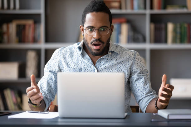 Frustrated young mixed race guy worrying of problem. Front view shocked millennial african american man in glasses looking at laptop screen, received email with unbelievable news. Frustrated young mixed race guy worrying of bad surprise or problem. shocked computer stock pictures, royalty-free photos & images