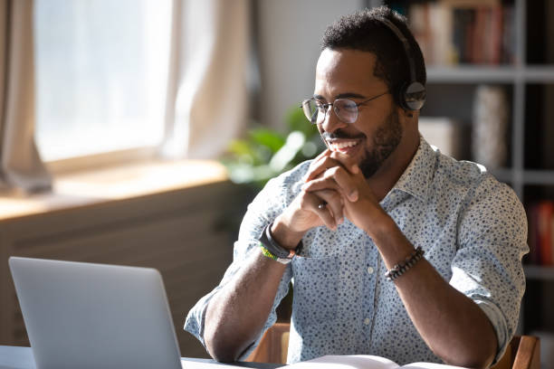 Smiling biracial businessman holding video call with clients partners. Happy millennial african american man in glasses wearing headphones, enjoying watching educational webinar on laptop. Smiling young mixed race businessman holding video call with clients partners. Happy Customer stock pictures, royalty-free photos & images