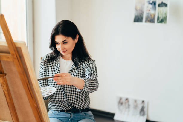 istock woman do easel drawing, holding brush in hand 1216970109