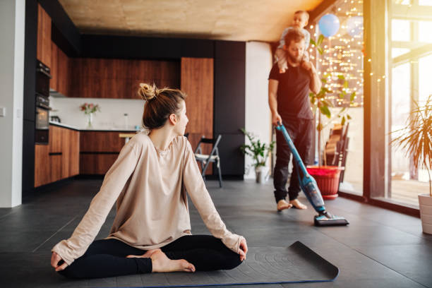 Family daily activity. child riding on father's neck. He vacuums, she does yoga. stock photo