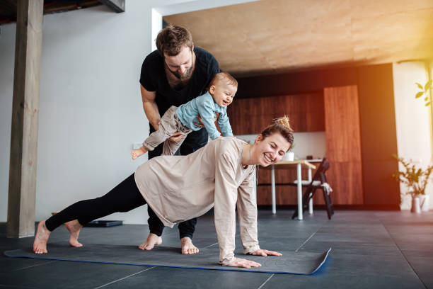 exercício matinal em família. mãe fazendo prancha, pai segurando bebê nas costas - child exercising sport yoga - fotografias e filmes do acervo