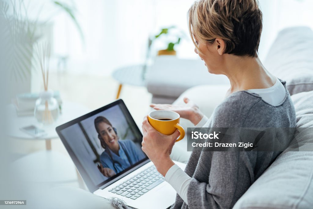 Frau mit Laptop und Videoanruf mit ihrem Arzt, während zu Hause sitzen. - Lizenzfrei Telemedizin Stock-Foto