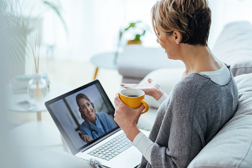 Mujer usando computadora portátil y haciendo videollamada con su médico mientras estaba sentada en casa. photo