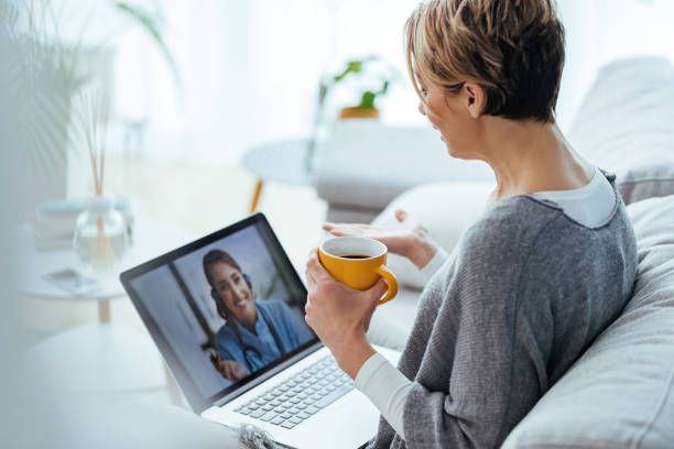 Woman using laptop and having video call with her doctor while sitting at home. Woman sitting on the sofa while making video call over laptop with her doctor. telemedicine stock pictures, royalty-free photos & images