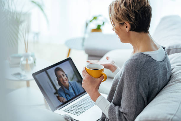 Woman using laptop and having video call with her doctor while sitting at home. Woman sitting on the sofa while making video call over laptop with her doctor. doctor utensils stock pictures, royalty-free photos & images