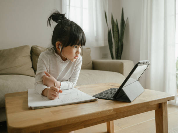 Little girl doing her homework with digital tablet. Young woman wearing headphones learning using digital tablet and teleconferencing apps in living room at home home schooling homework computer learning stock pictures, royalty-free photos & images
