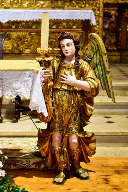Faro / Algarve, Portugal - 07.20.2019: Church of Carmo, an angel statue decorated with gold paint, with a candlestick and a burning candle.