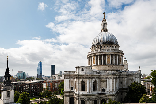 Side view of St. Paul’s Cathedral in London against a cloudy sky, with some modern skyscrapers in the background.