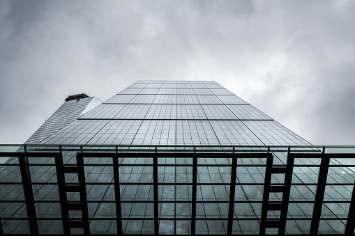 Low-angle view of a modern glass office building against a cloudy sky in London, UK.