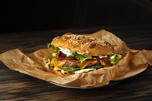 Appetizing hamburger with meat and vegetables on food paper with peppers