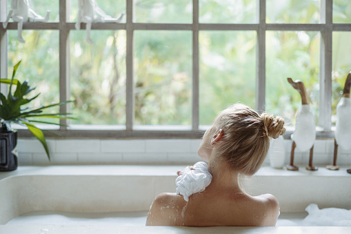 Joven mujer adulta tomando baño sosteniendo esponja en la mano, hombro lavado photo