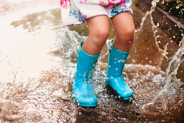 menina alegre se divertindo em poça na rua - wet dress rain clothing - fotografias e filmes do acervo