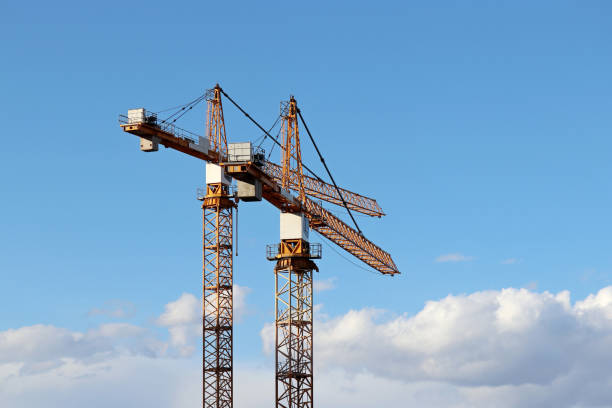 istock Two construction cranes on background of blue sky and white clouds 1216989647