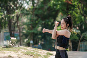 Portrait rear of an Asian woman wearing a black sports bra and she is body warm up for a workout by running in the park. Urban health care concept.