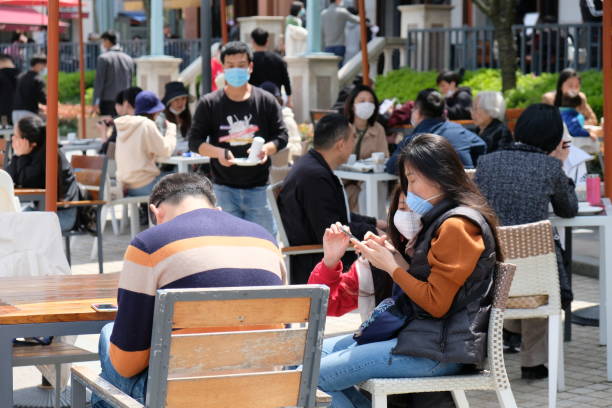 Crowd of people wearing protective mask, sitting at outdoor restaurant Suzhou/China-April 2020: life returns to normal in many cities in China. Crowd of people sitting at outdoor restaurant, wearing protective mask to prevent coronavirus chinese ethnicity china restaurant eating stock pictures, royalty-free photos & images