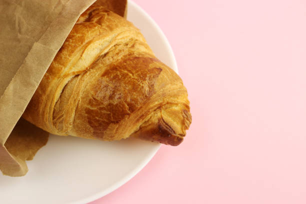 istock Croissant in a paper bag on a plate on a pink background 1216992121
