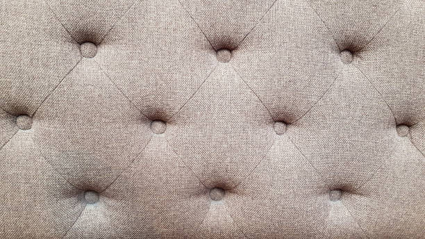 Textured fabric surface of upholstered furniture. Rhombus pattern of grey sofa tightened with round buttons on soft textile background. Interior upholstery backdrop. stock photo
