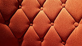 Orange color fabric surface of upholstered furniture. Rhombus pattern sofa tightened with round buttons on soft textile background. Interior upholstery.