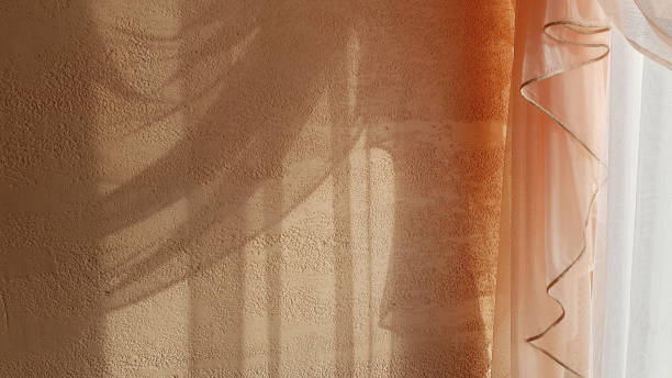 istock Transparent shadows from draped tulle curtain on beige textured plaster wall background. Wavy textile frill textures. Light and shadow monochrome backdrop with copy space. 1216997063