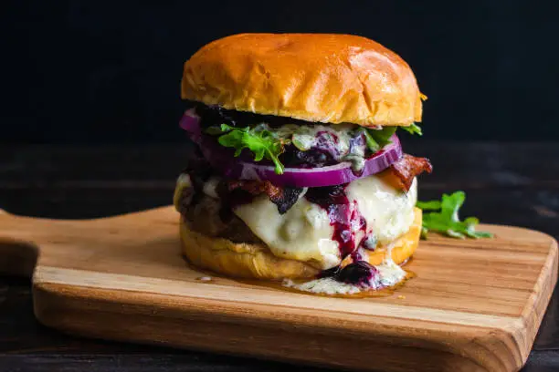 Bacon cheeseburger topped with Havarti cheese, blueberry compote, red onion, arugula, and basil aioli