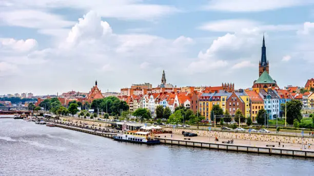 Ships anchored on Odra River pier. People relaxing on Piastowski Boulevard. Cathedral Basilica of St James the Apostle in background, Szczecin, Poland