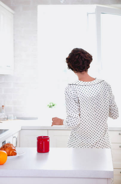 istock Woman looking out window while standing in light modern kitchen at home in daytime 1217001889