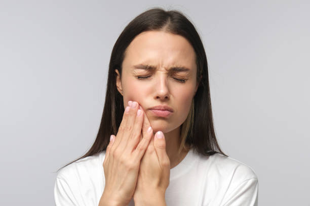 Young miserable woman experiencing severe toothache, pressing palm to cheek, closing eyes because of strong pain, isolated on gray background Young miserable woman experiencing severe toothache, pressing palm to cheek, closing eyes because of strong pain, isolated on gray background jaw pain stock pictures, royalty-free photos & images